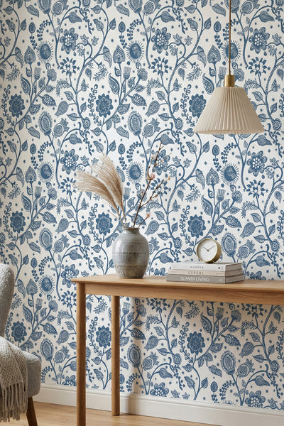 Blue folk-art blooms and vines on a light Scandinavian wallpaper in a reading corner.