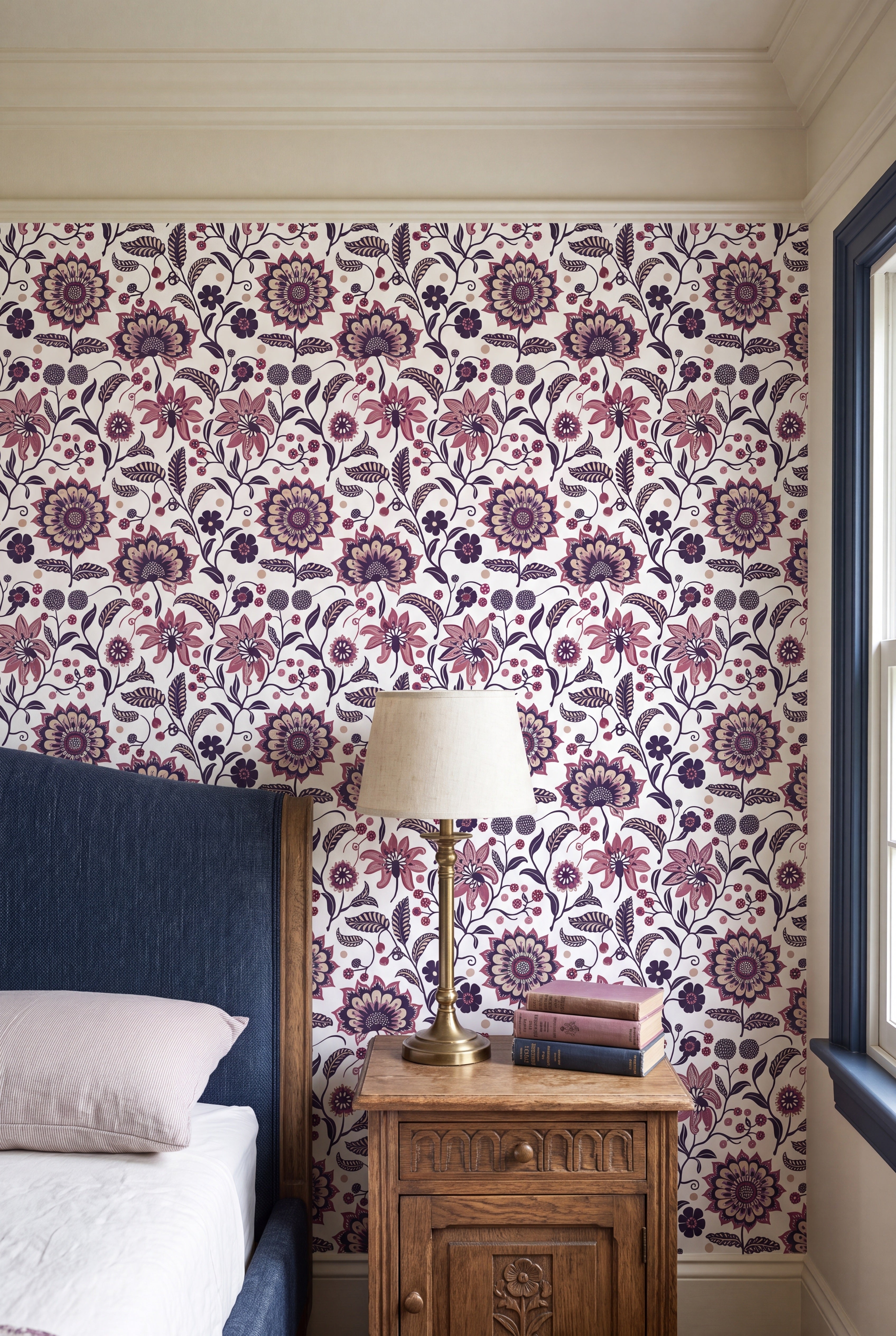 Plum and blush folk blooms and vines on soft white wallpaper in a bedroom.