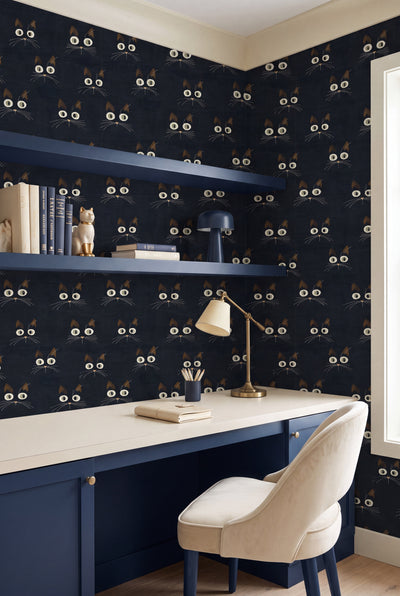 Whimsical cream and pink cat faces on black wallpaper in a home office.