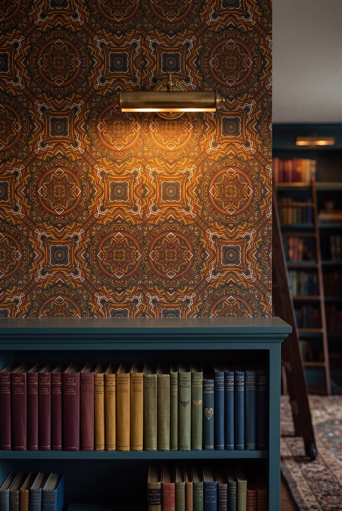 Caravan Mandala wallpaper in rust, teal and gold on dark brown on a library wall.